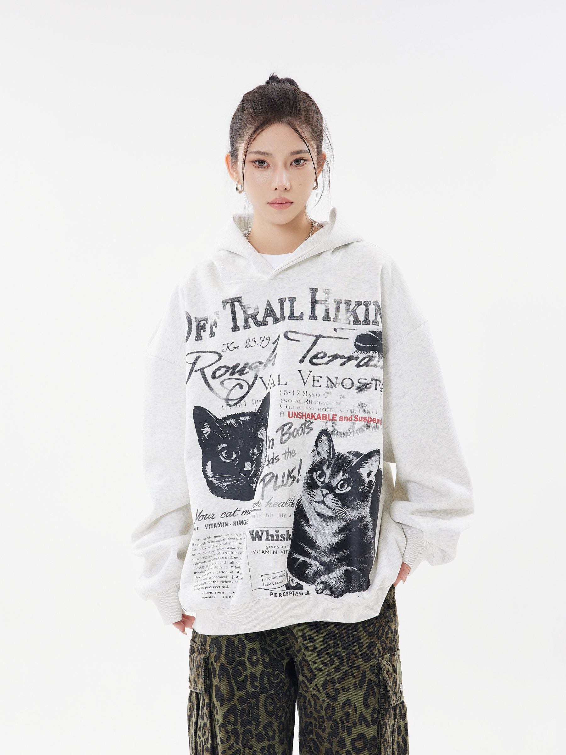 Model wearing Oatmeal Heather oversized hoodie with vintage cat graphic and Off Trail Hiking text, styled with camo pants.
