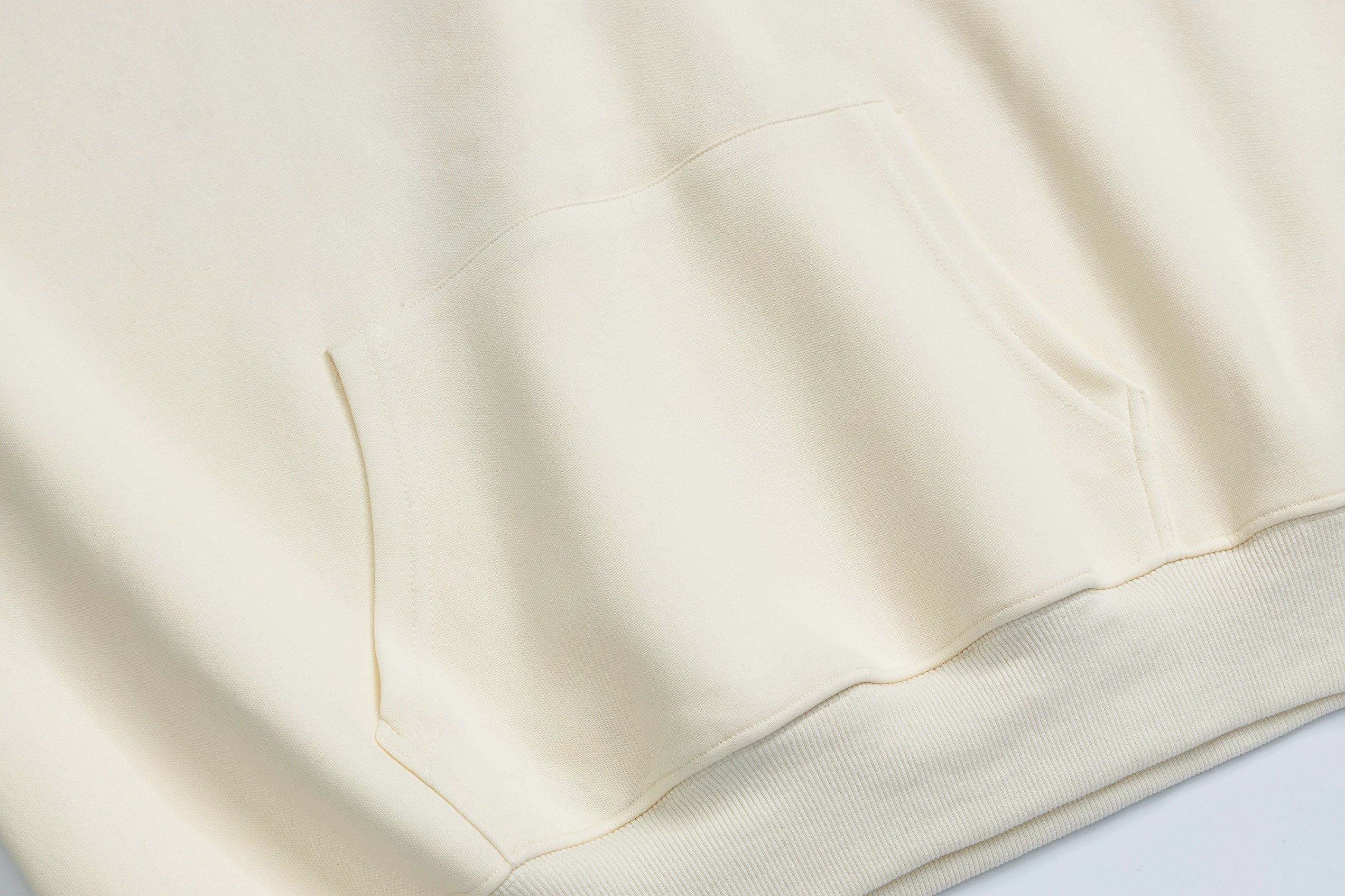 Close-up of the kangaroo pocket on a cream oversized hoodie showing soft fabric texture and stitching details.