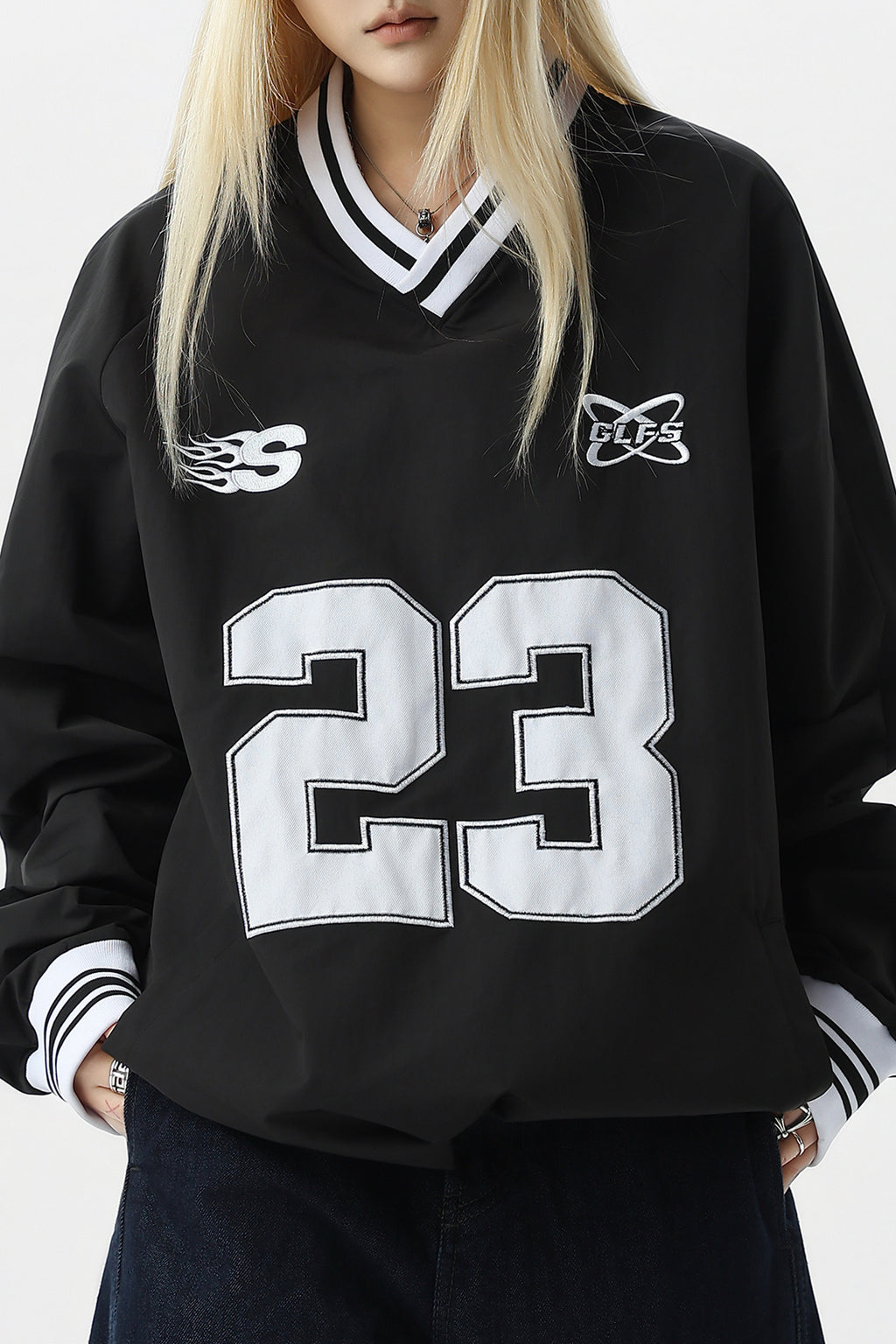 Model wearing black V-neck pullover jacket with white embroidery.