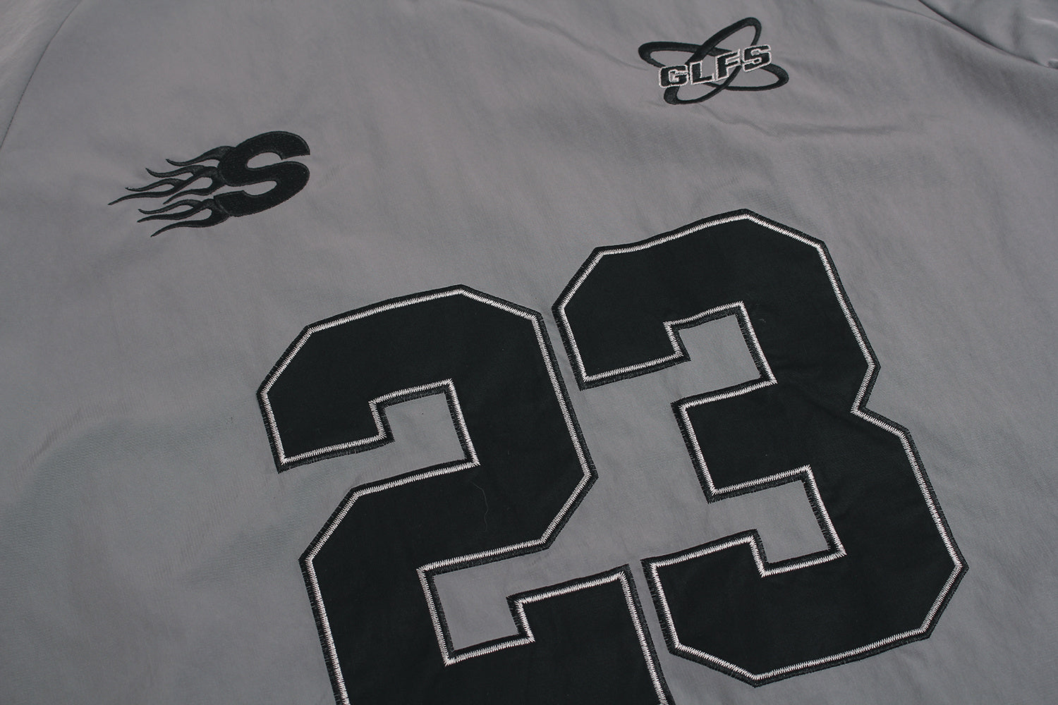 Close up of embroidered GLFS logo on grey waterproof windbreaker.