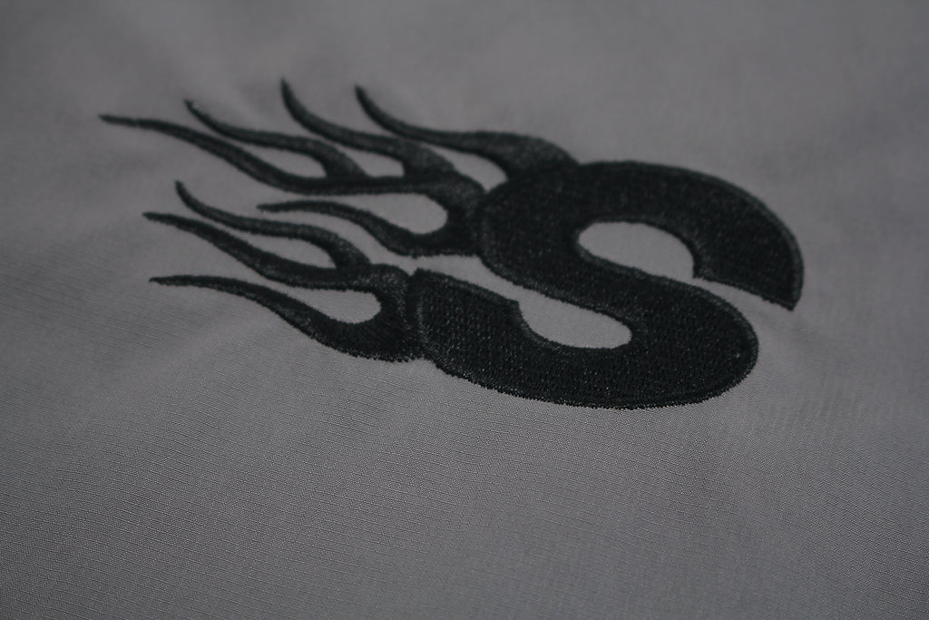 Close up of embroidered GLFS logo on grey waterproof windbreaker.