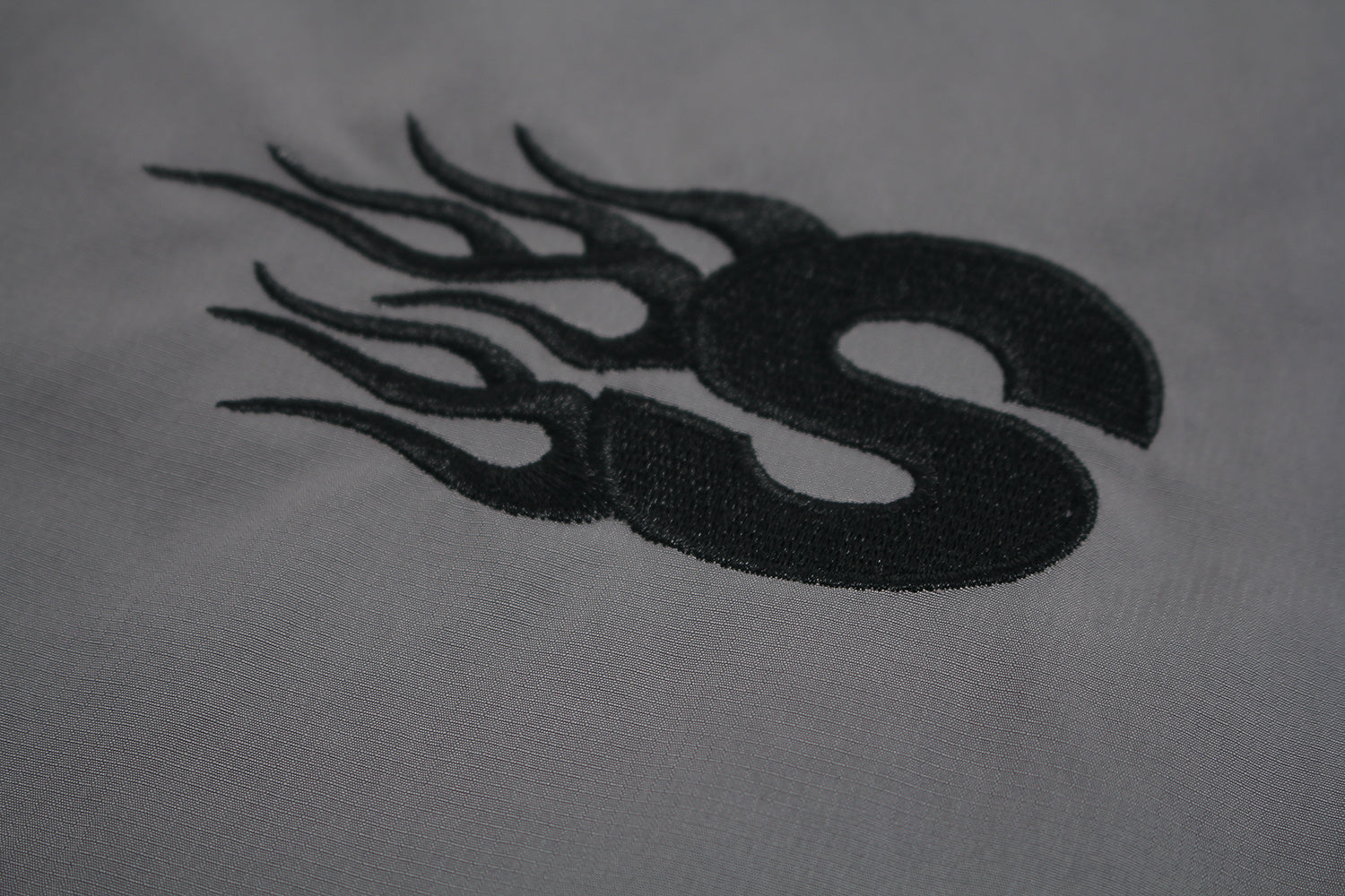 Close up of embroidered GLFS logo on grey waterproof windbreaker.