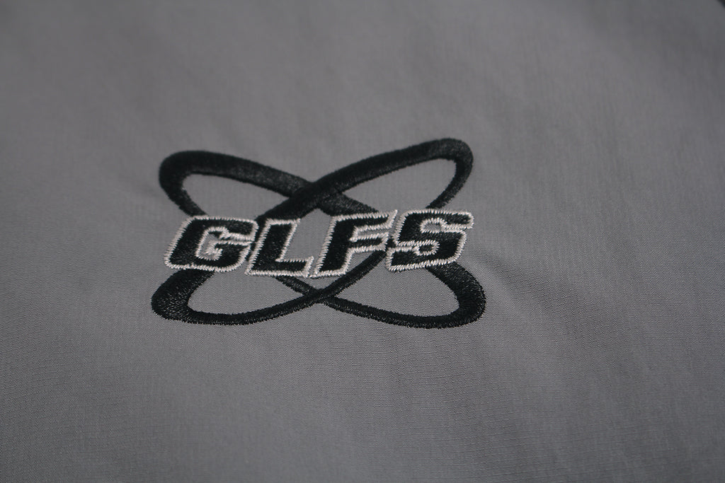 Close up of embroidered GLFS logo on grey waterproof windbreaker.
